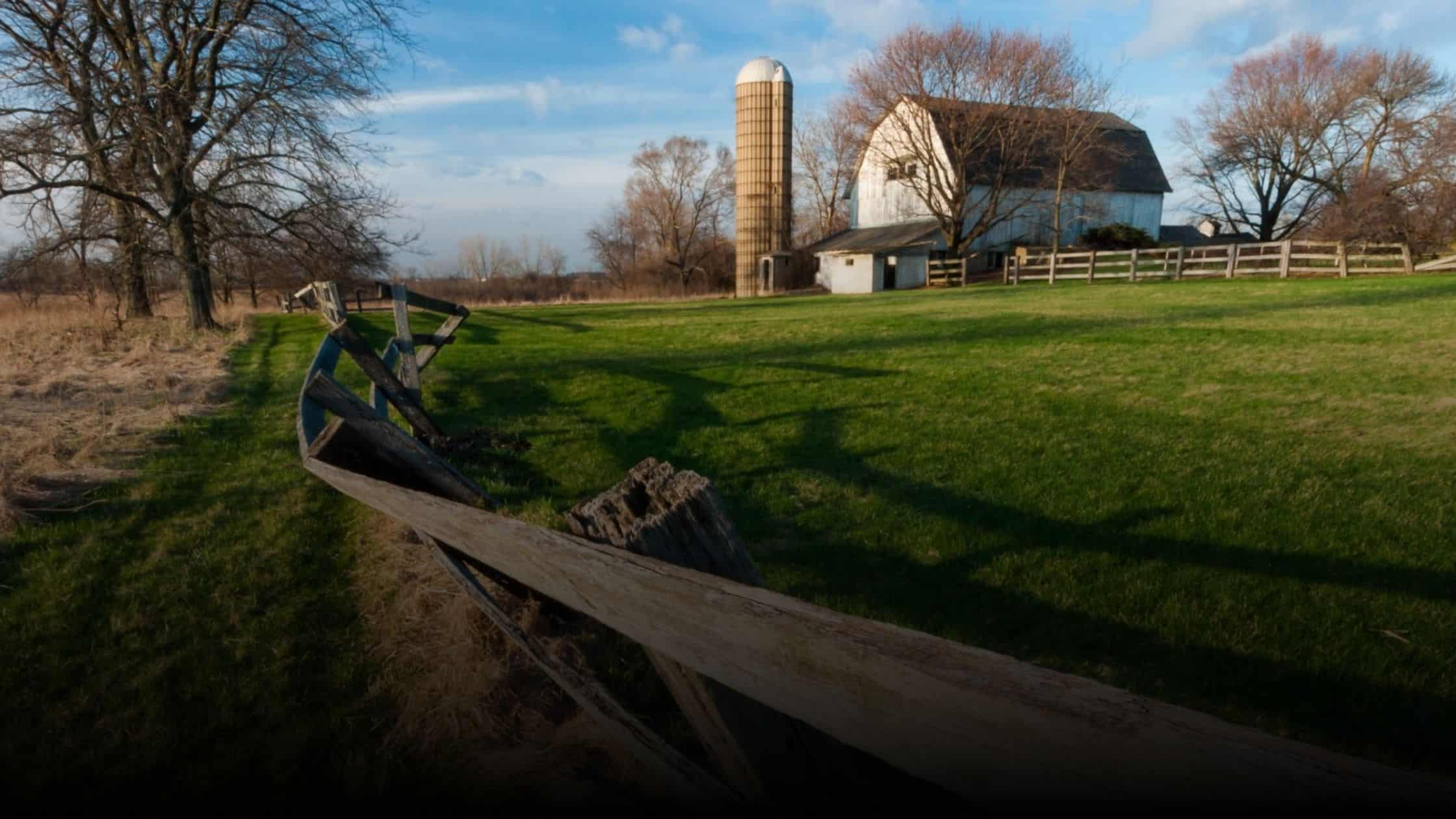 A scenic barn in Wayne, Illinois, with a silo and rustic fence surrounded by open fields and bare trees in early spring